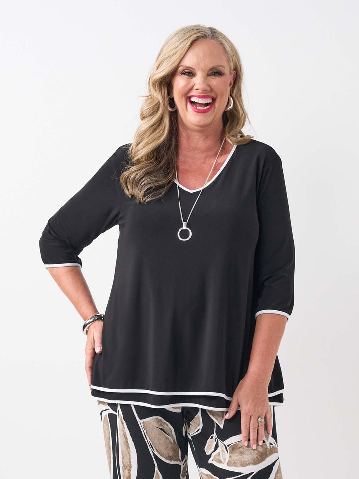 a woman wearing a plain black v-neck swing layered top with contrast white trim