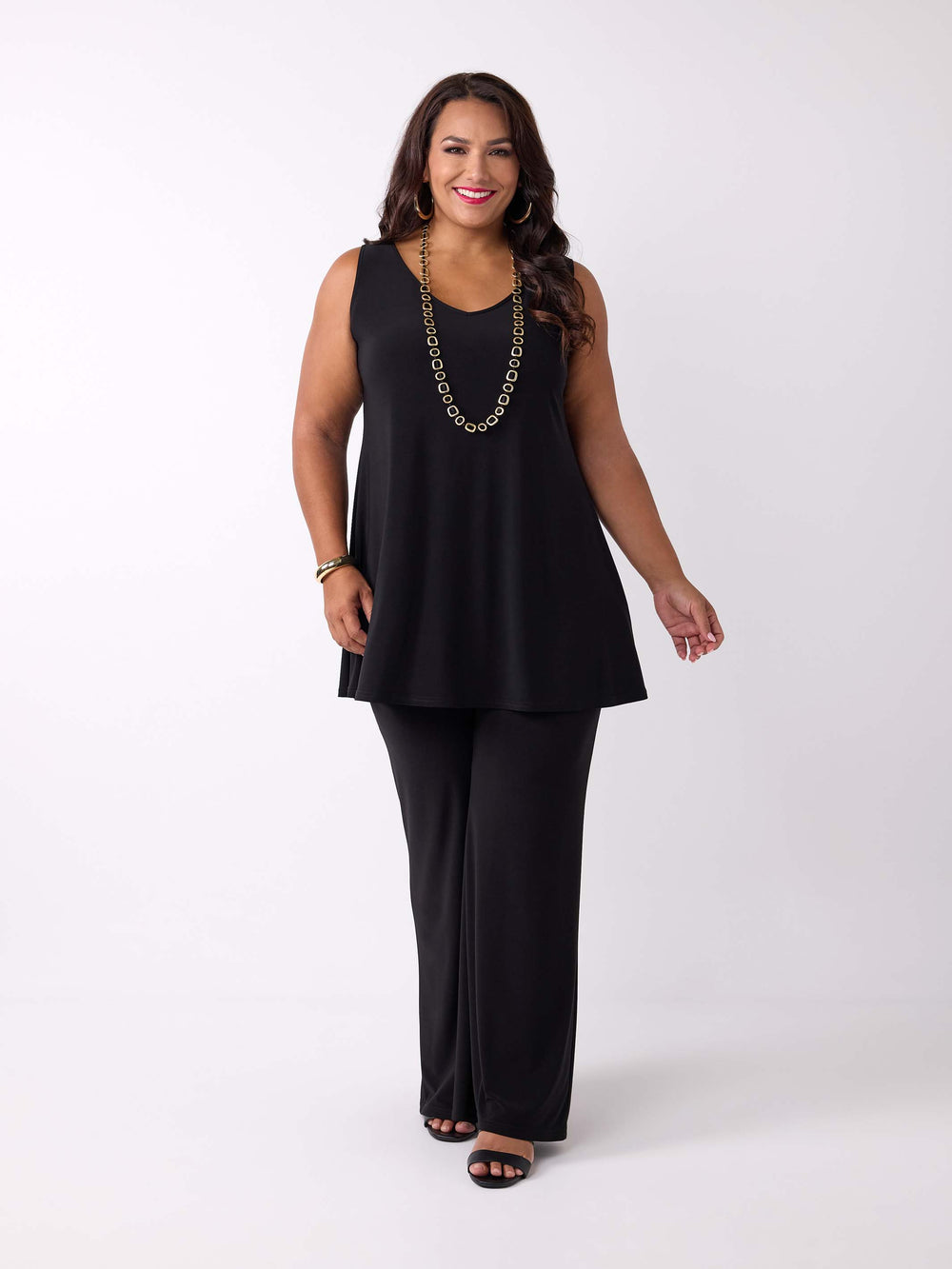 A woman modeling a black sleeveless v-neck tunic cami top paired with matching black wide-leg pants