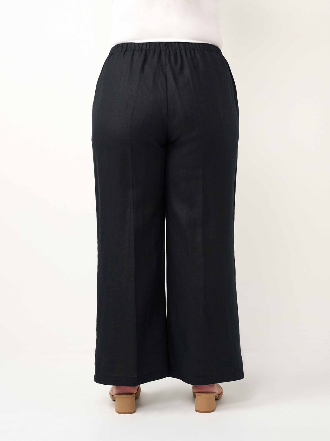 Black wide-leg cropped pants shown from the back on a model, featuring an elastic waistband and a straight, relaxed leg silhouette.