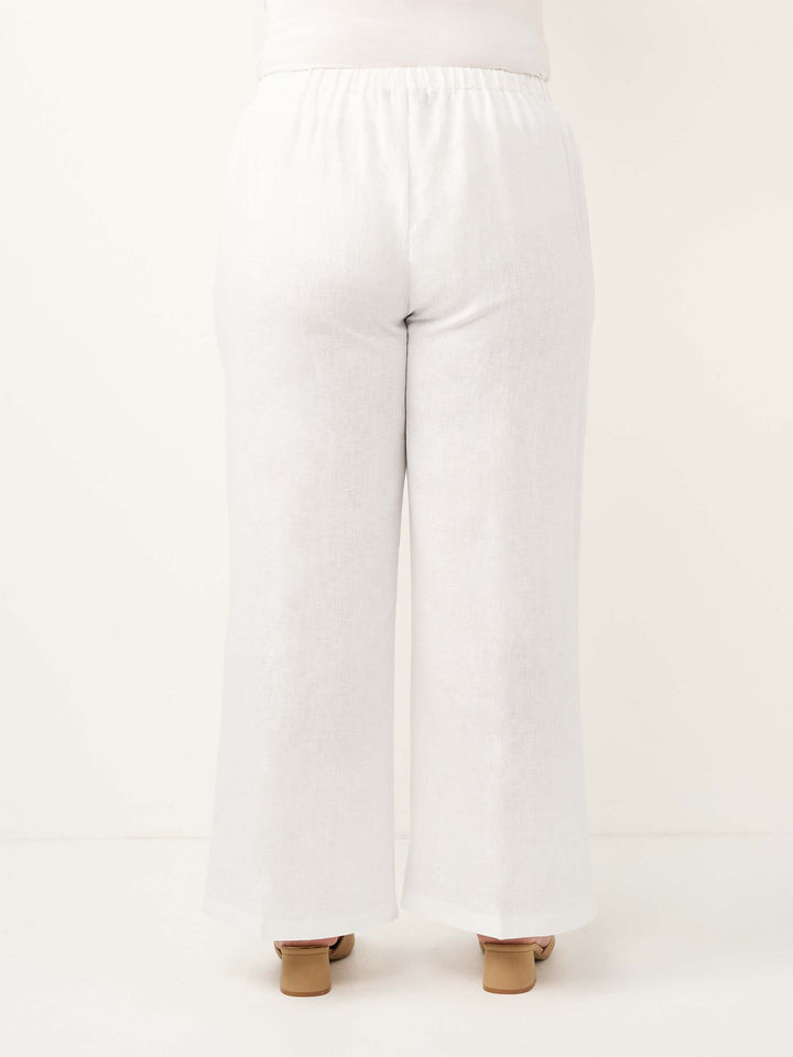 White wide-leg linen pants shown from the back on a model, featuring an elastic waistband and a straight, relaxed leg.