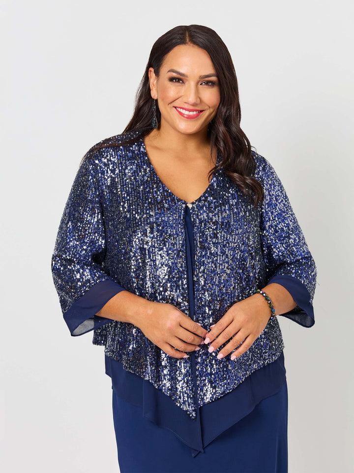 A woman wearing a navy blue sequined evening jacket with three-quarter sleeves and a draped waist, paired with a navy dress