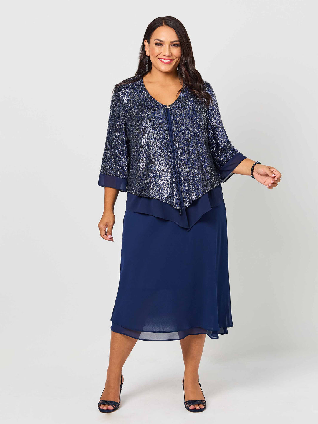 A woman wearing a navy blue sequined evening jacket with three-quarter sleeves and a draped waist, paired with a navy dress