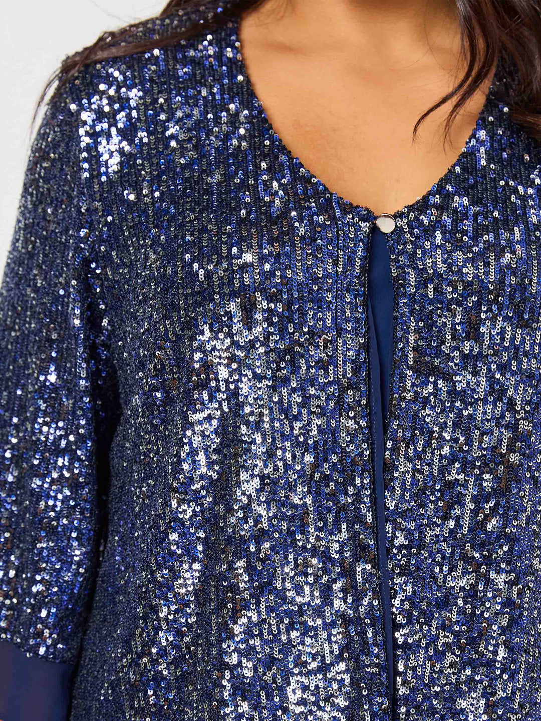 Close-up of a person wearing a sparkling blue sequined top with a V-neckline and a small decorative button at the collar.