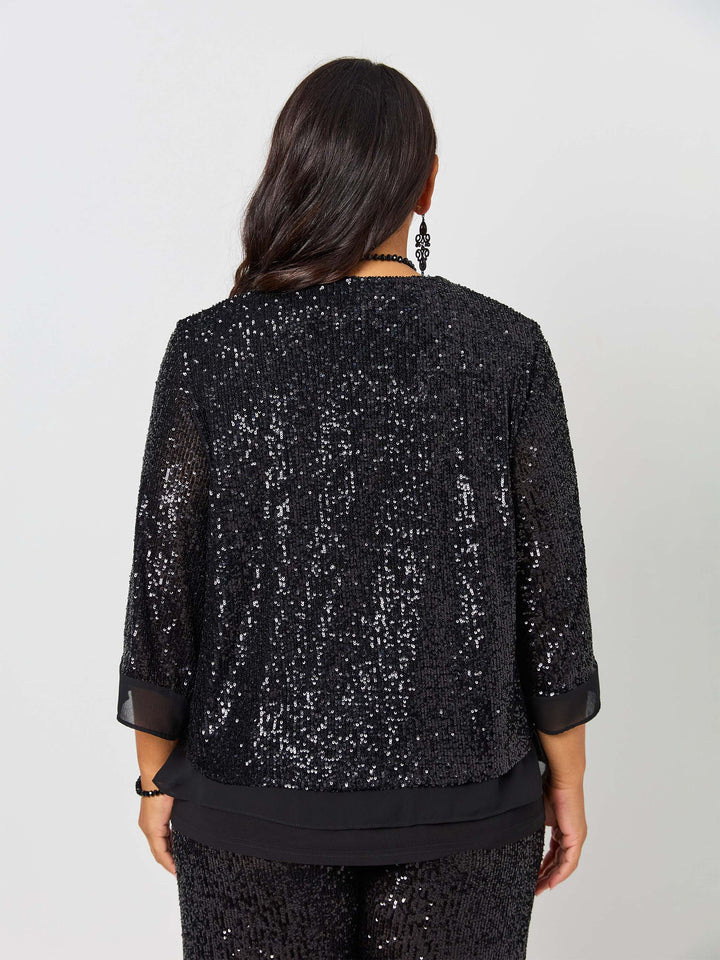 A woman viewed from the back wearing a black sequined three-quartered sleeve evening jacket with sheer cuffs and a layered black hem, paired with matching black sequined pants