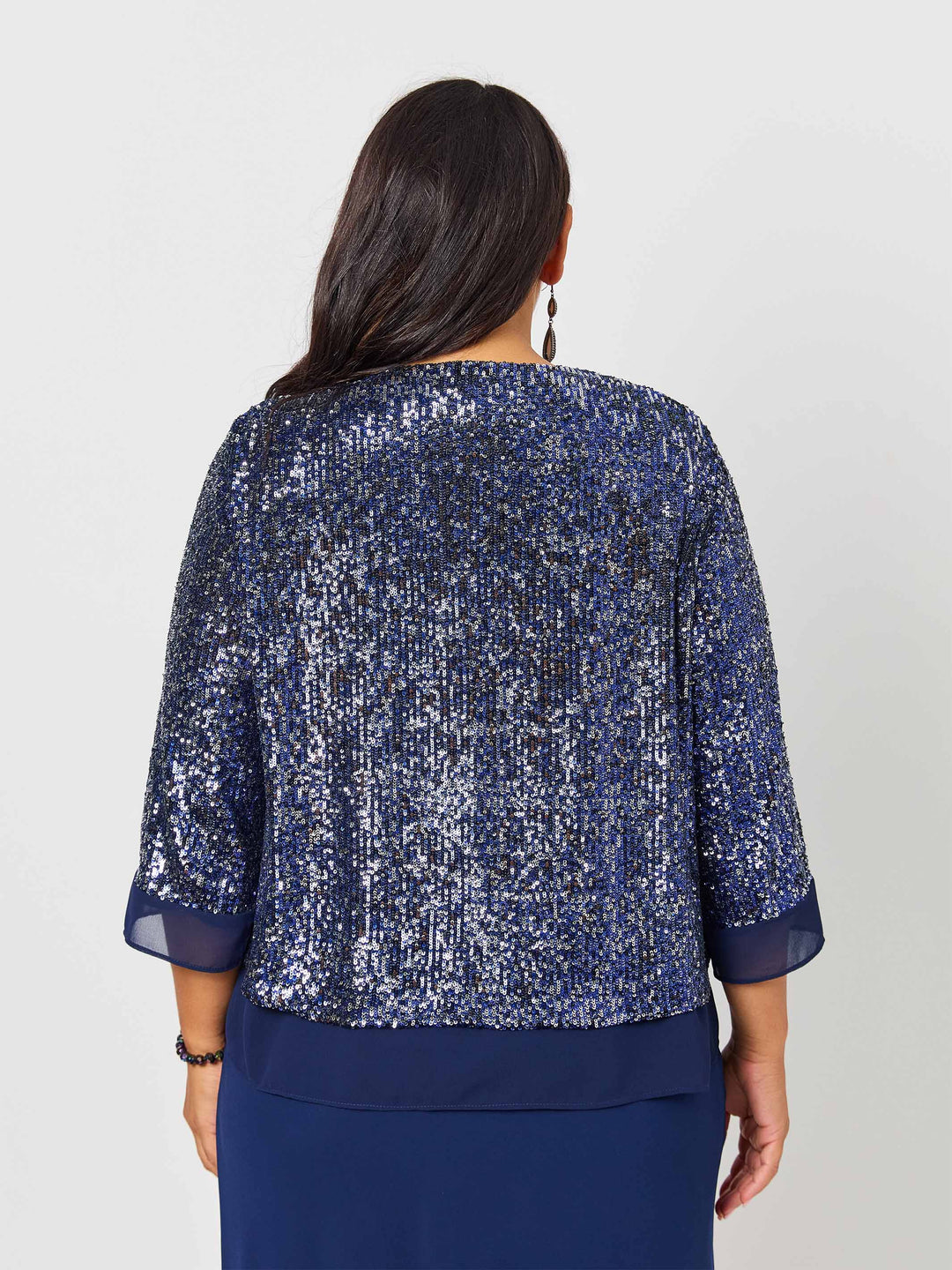 A woman wearing a navy blue sequined evening jacket with three-quarter sleeves and a draped waist, paired with a navy dress