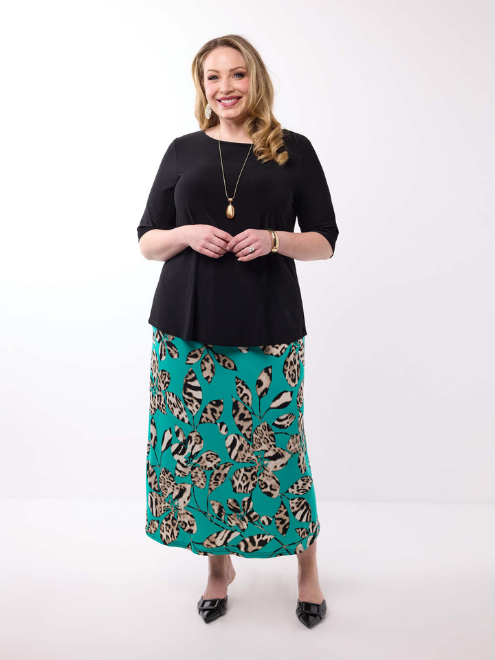 A woman wearing a black short-sleeve top paired with a teal green midi skirt featuring a leopard print