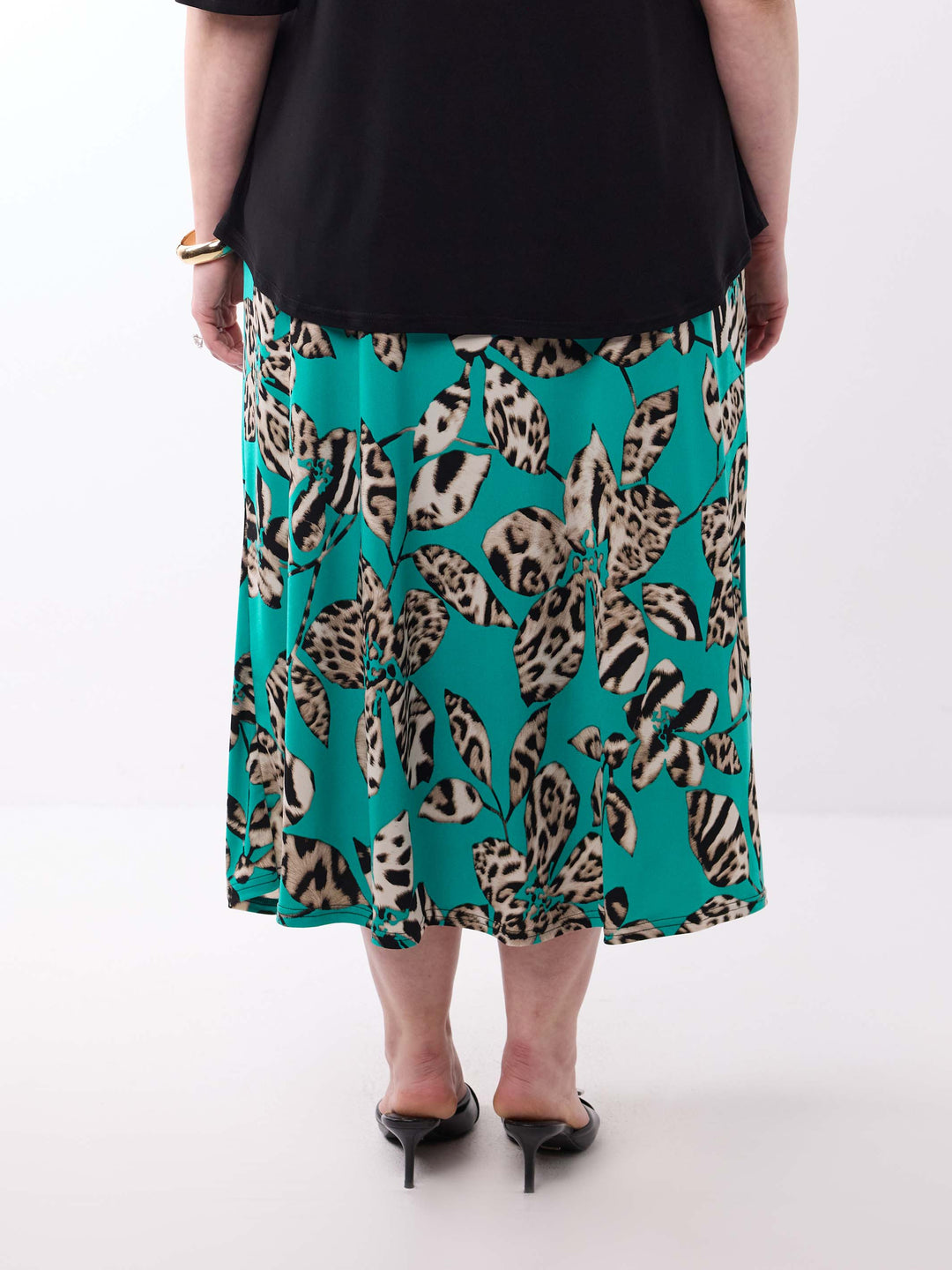 A person shown from the back wearing a black top and a teal midi skirt with a bold leopard leaf print