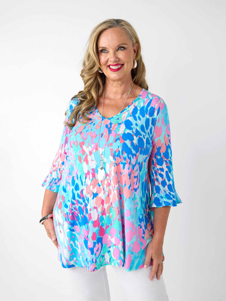 A woman wearing a v-neck top with 3 quarter frill sleeves in aqua blue and pink print