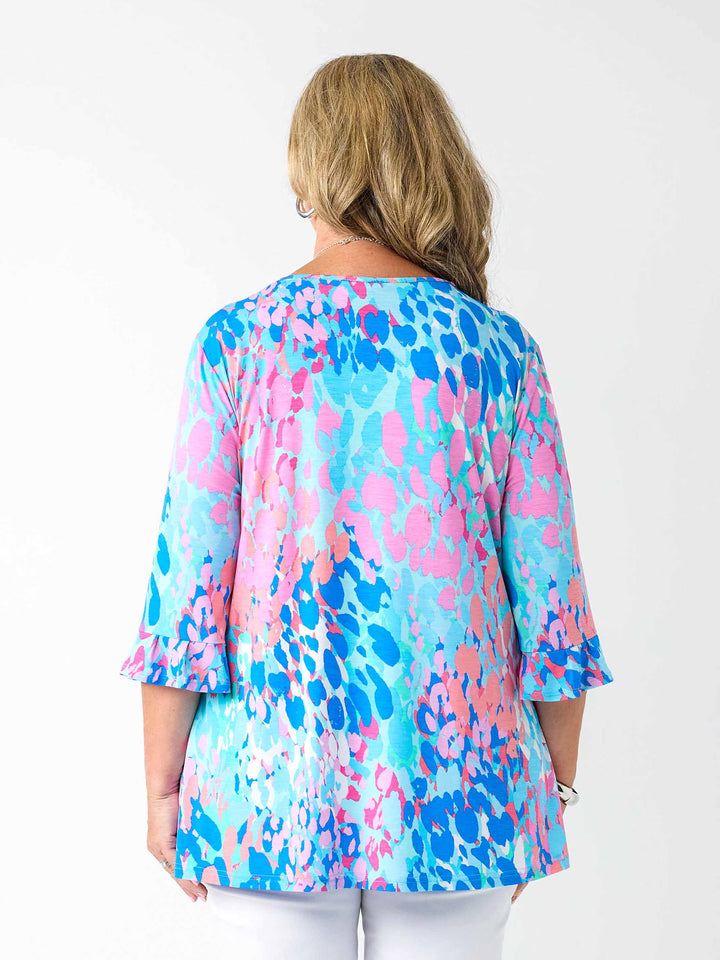 Back view of a woman wearing a v-neck top with 3 quarter frill sleeves in aqua blue and pink print, paired with white pant