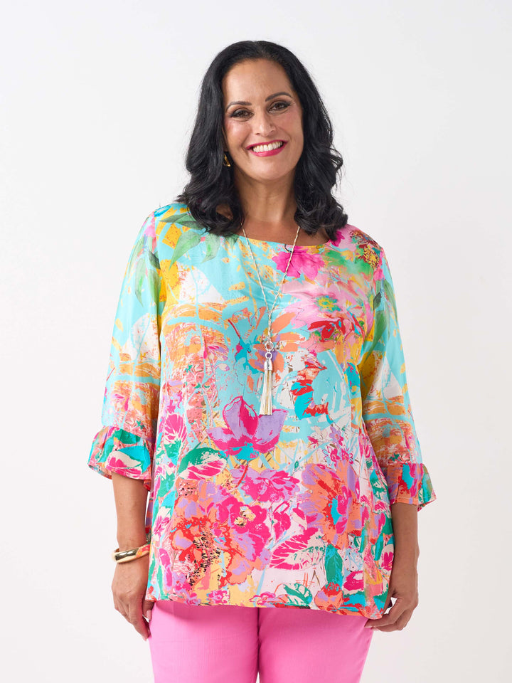 A woman wearing a vibrant floral printed top with three-quarter length frill cuff.