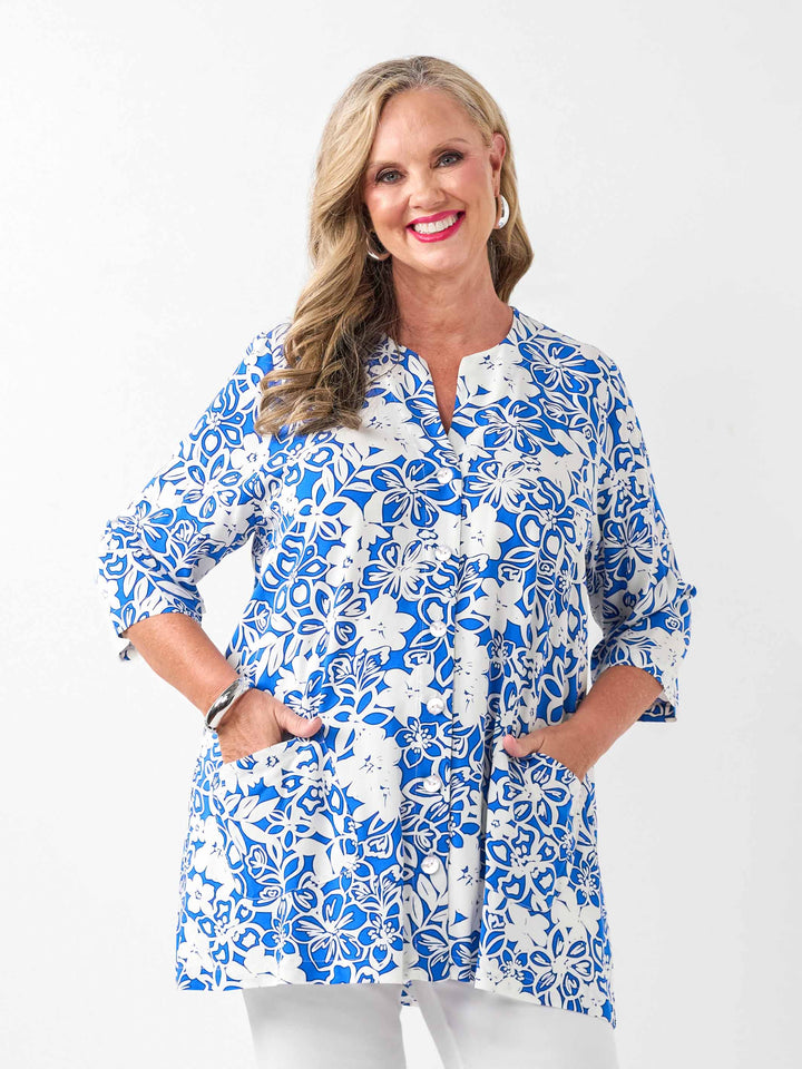 A woman wearing a blue and white floral print tunic top with white pants