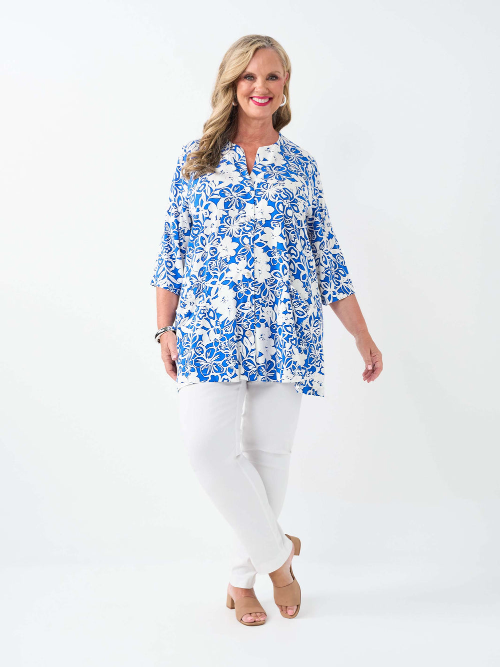 A woman wearing a blue and white floral print tunic top with white pants