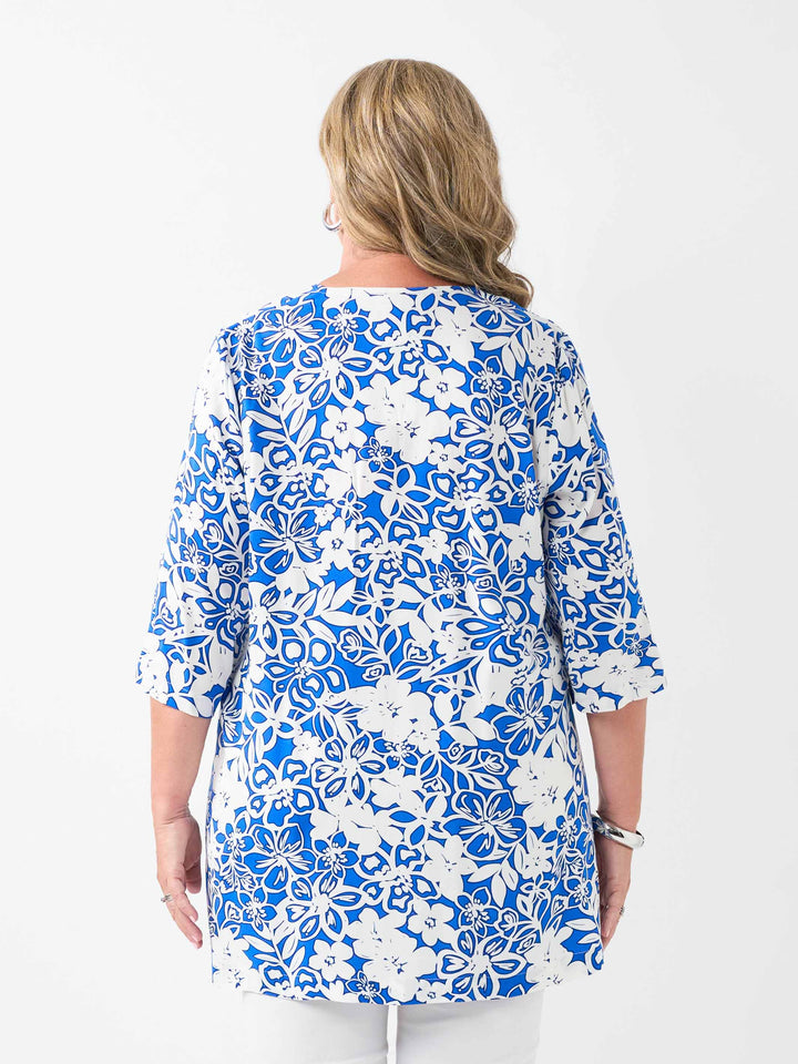 A back view of a woman wearing a blue and white floral print tunic top with white pants