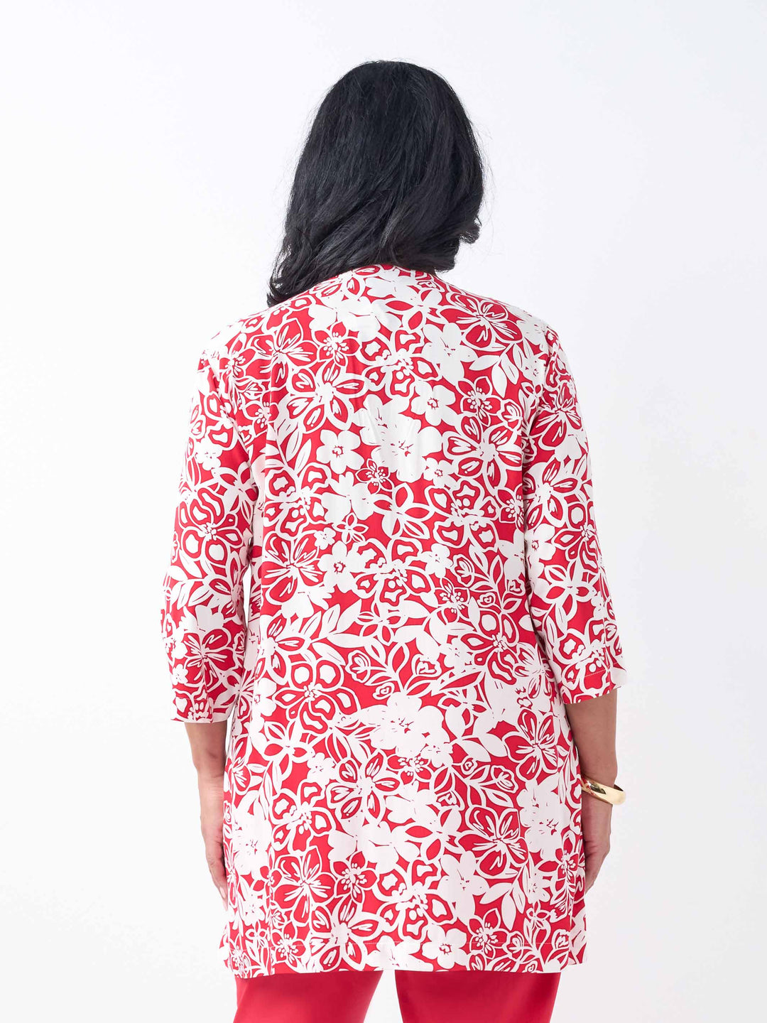 A back view of a woman wearing a red and white floral print tunic top with three-quarter sleeves, paired with red pants