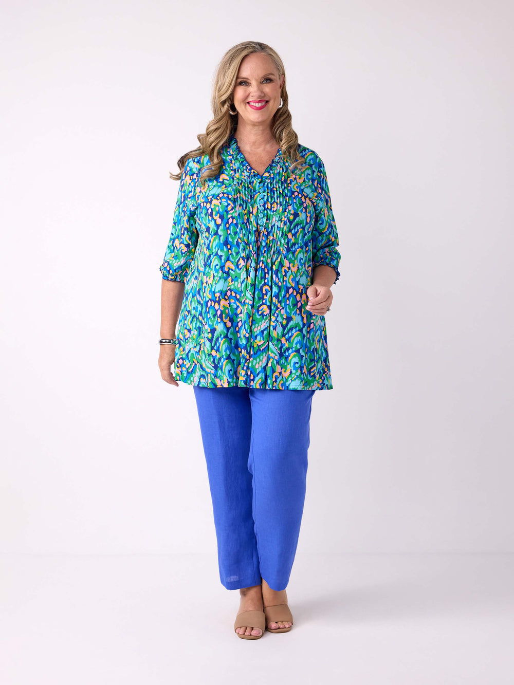 A woman wearing a colourful abstract print tunic top with blue pants