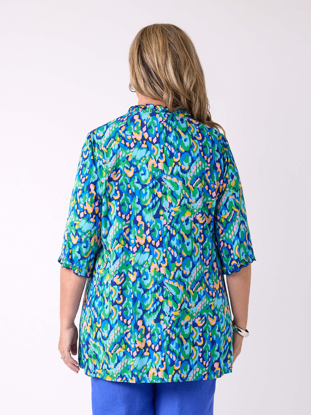A woman viewed from the back wearing a colourful abstract print tunic top with blue pants
