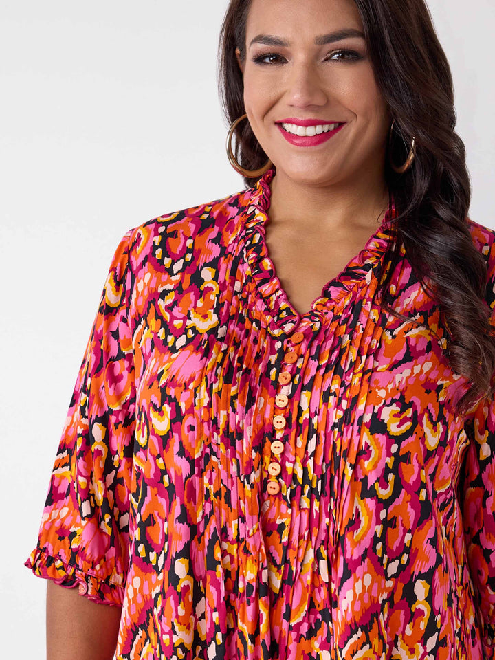 A woman wearing a vibrant, multicolour abstract print top with three-quarter ruffled sleeves and a smocked neckline