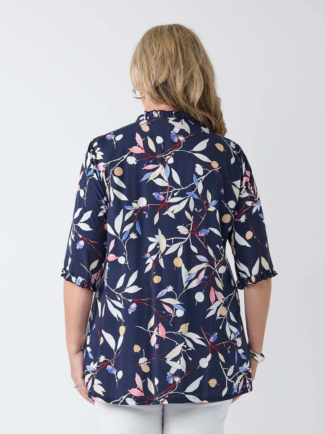 A woman viewed from the back wearing a navy blue short-sleeve blouse with a white, pink, and blue floral leaf print, paired with white pants.