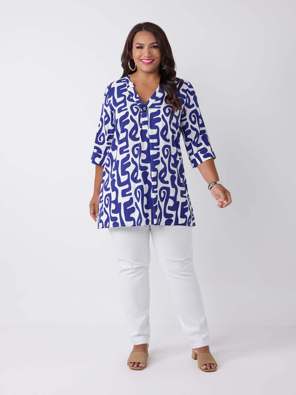 A woman wearing a blue and white abstract patterned v-neck blouse with three-quarter sleeves and a big button, paired with white pants