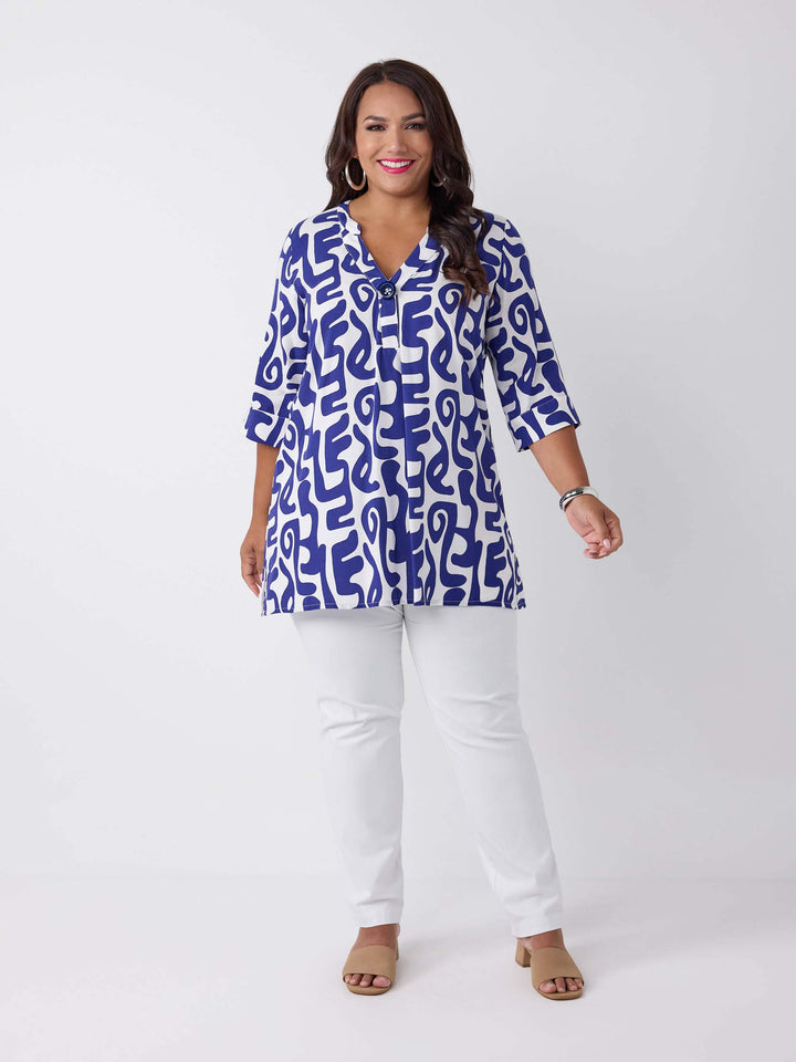 A woman wearing a blue and white abstract patterned v-neck blouse with three-quarter sleeves and a big button, paired with white pants