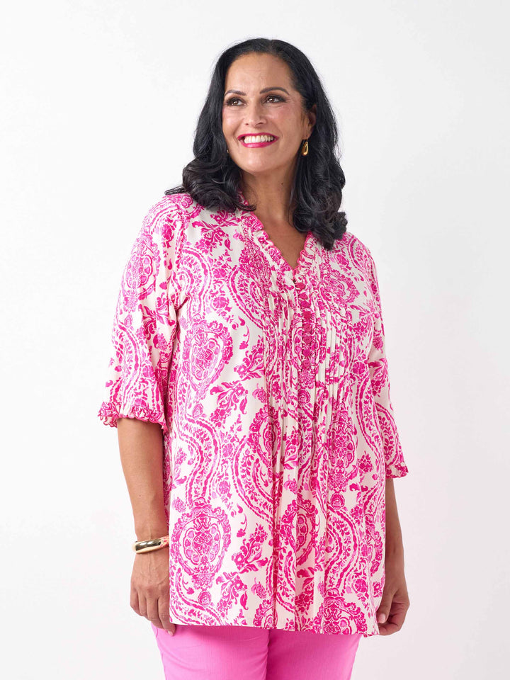 A woman wearing a pink and white paisley print tunic top with pinktucked front and three-quarter ruffled sleeves, paired with pink pants