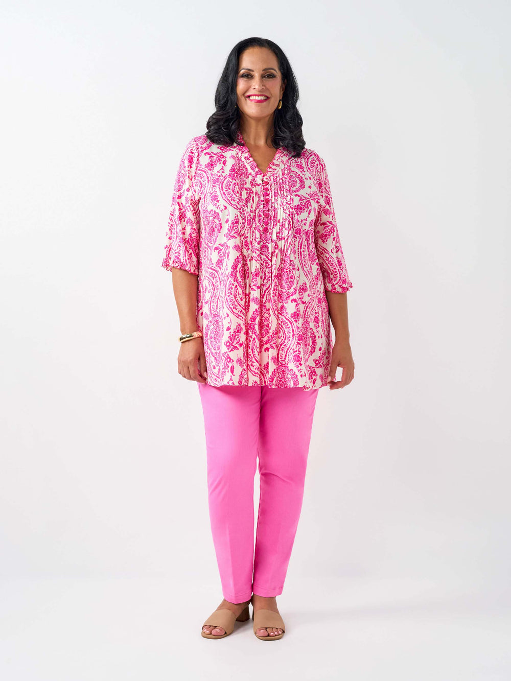 A woman wearing a pink and white paisley print tunic top with pinktucked front and three-quarter ruffled sleeves, paired with pink pants