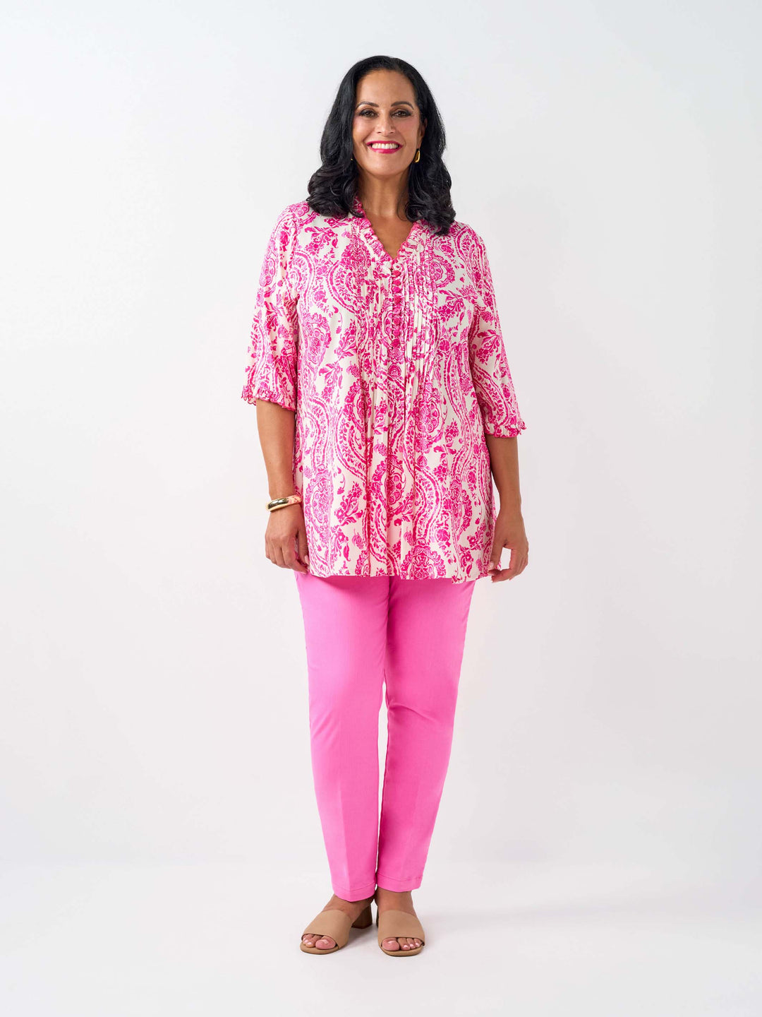 A woman wearing a pink and white paisley print tunic top with pinktucked front and three-quarter ruffled sleeves, paired with pink pants