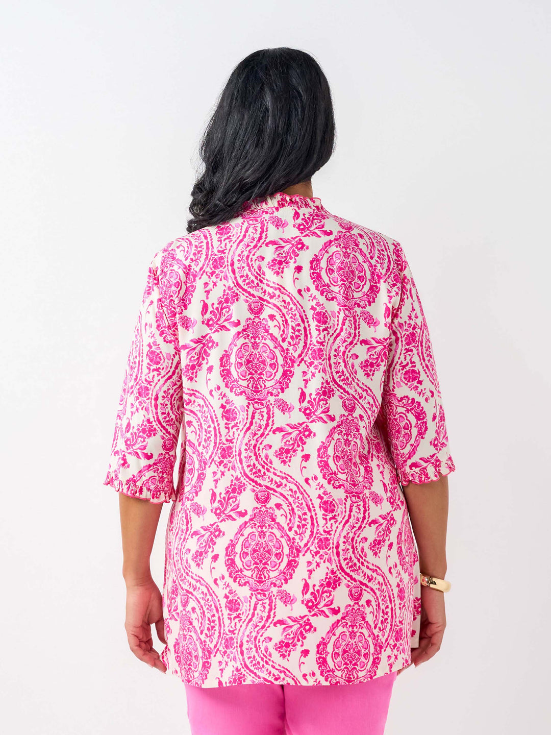 A woman viewed from the back wearing a pink and white paisley print tunic top with three-quarter ruffled sleeves, paired with pink pants