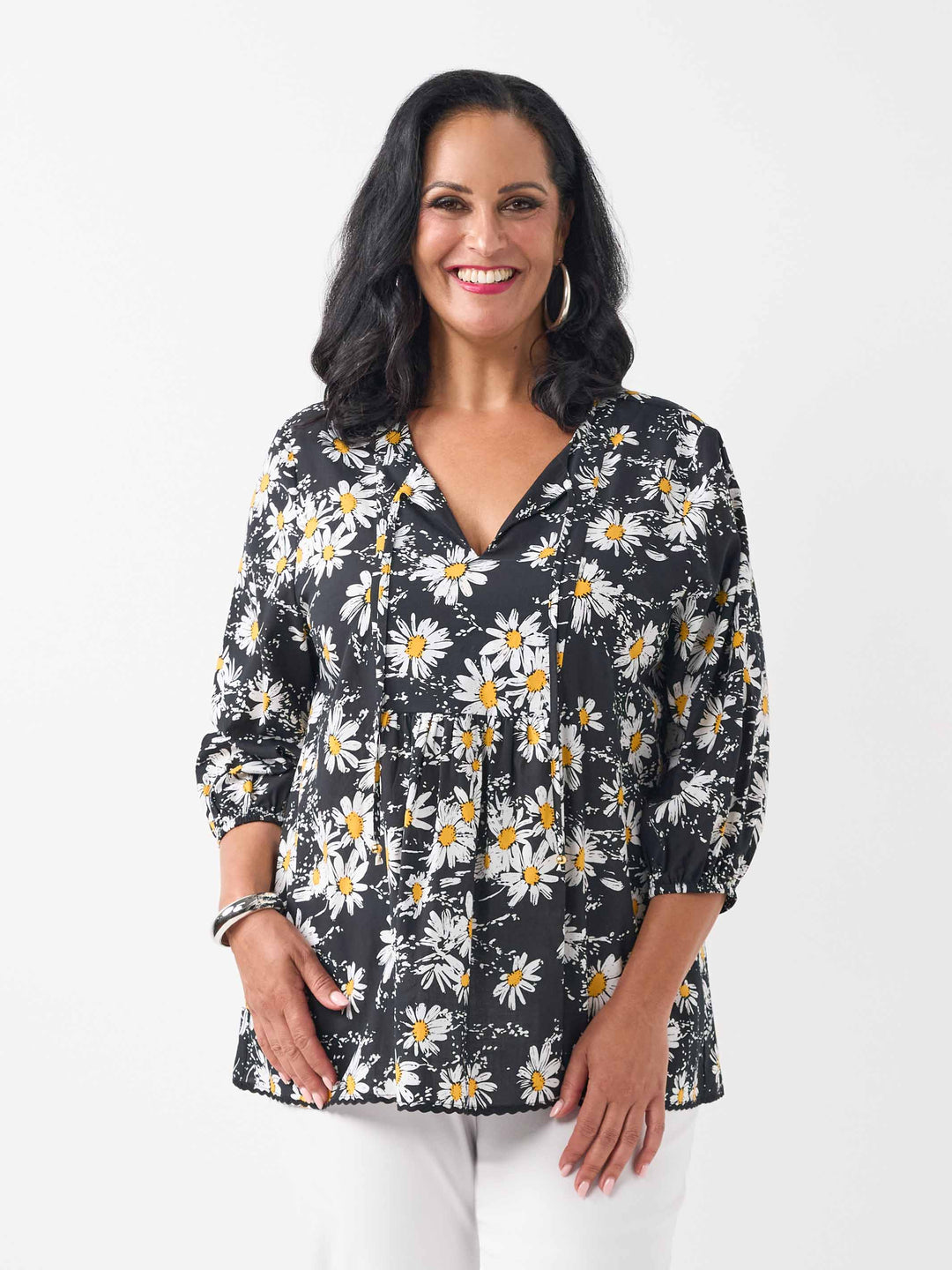 A woman wearing a black long-sleeve blouse with a white and yellow daisy floral print, paired with white pants