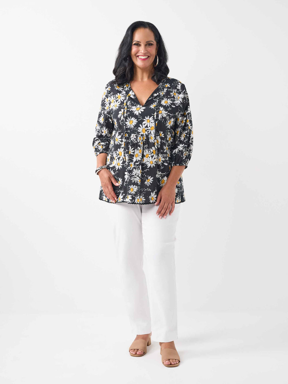 A woman wearing a black long-sleeve blouse with a white and yellow daisy floral print, paired with white pants