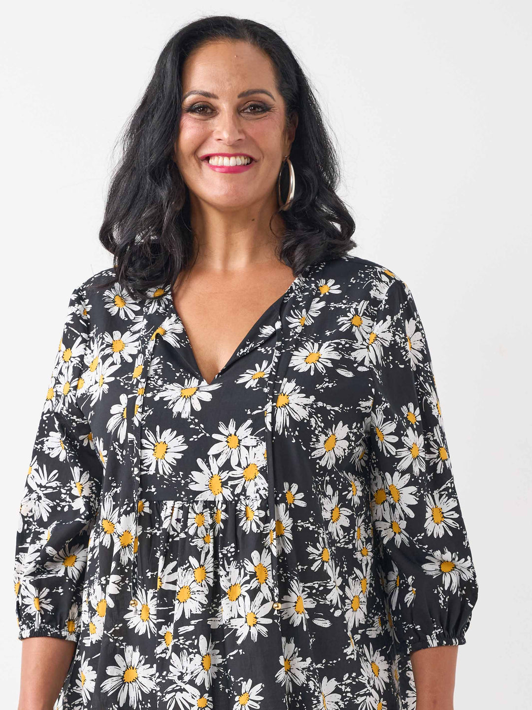 A detail view of a woman wearing a black long-sleeve blouse with a white and yellow daisy floral print, paired with white pants