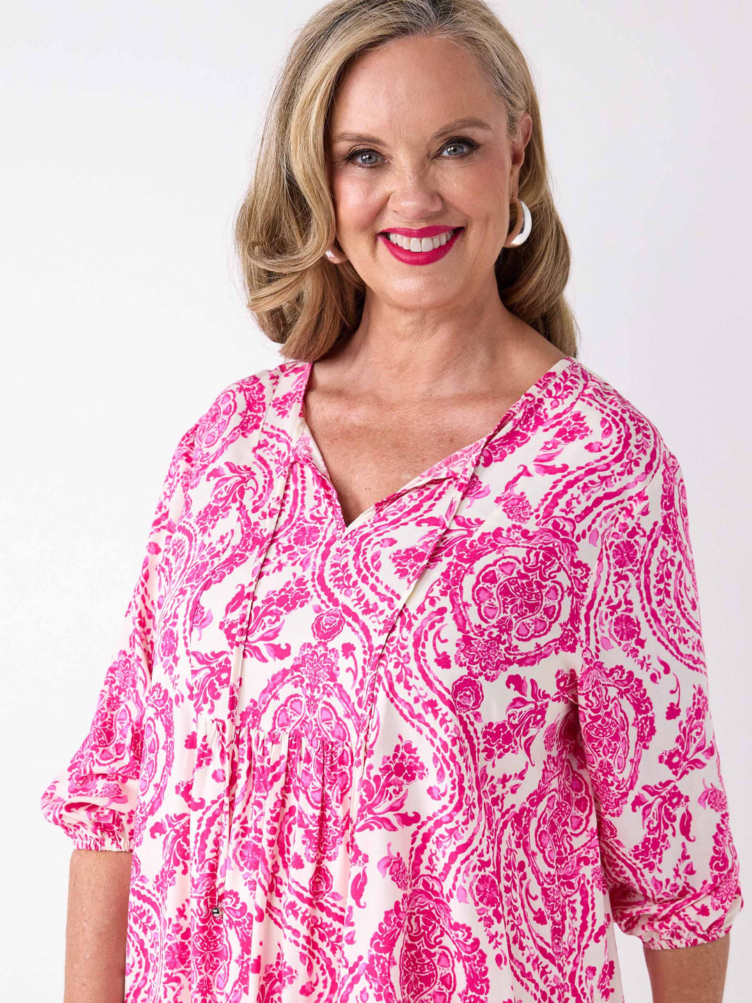 A woman wearing a pink and white paisley patterned blouse with v-neck tie front and three-quarter sleeves