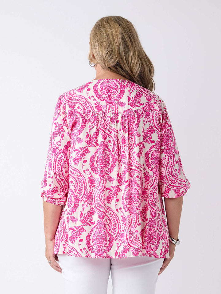 A woman viewed from the back wearing a pink and white paisley patterned blouse with three-quarter sleeves, paired with white pants