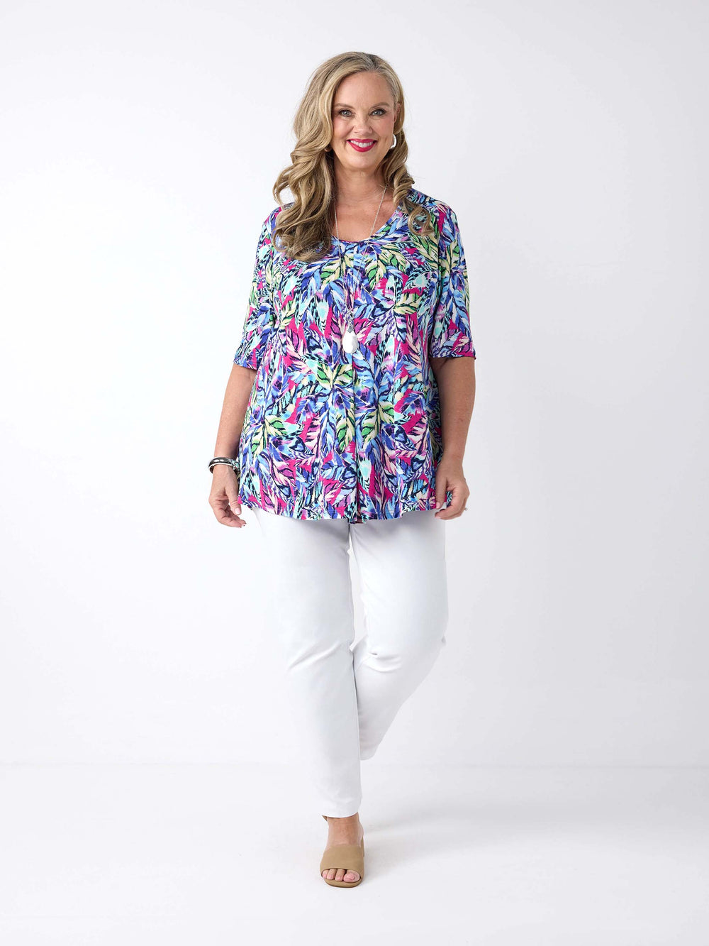 a woman wearing a summer top with vibrant tropical print in navy and pink, paired with white pant