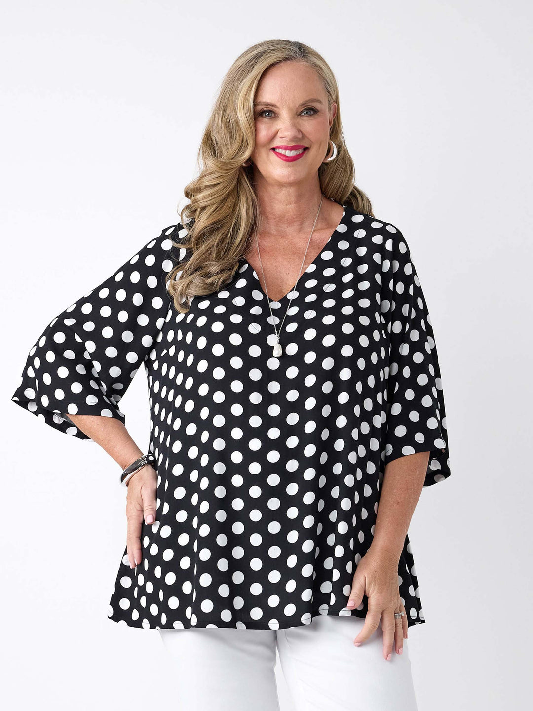 A woman wearing a black V-neck top with white polka dot with three-quarter sleeves, paired with white pants
