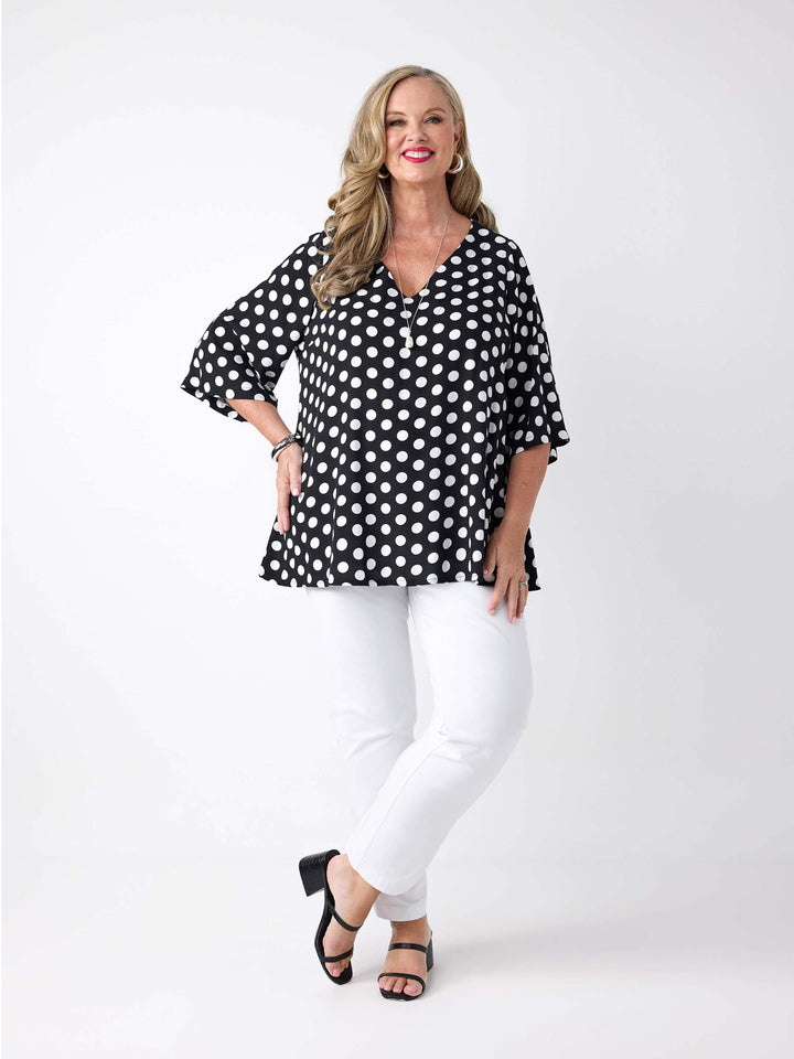 A woman wearing a black V-neck top with white polka dot with three-quarter sleeves, paired with white pants
