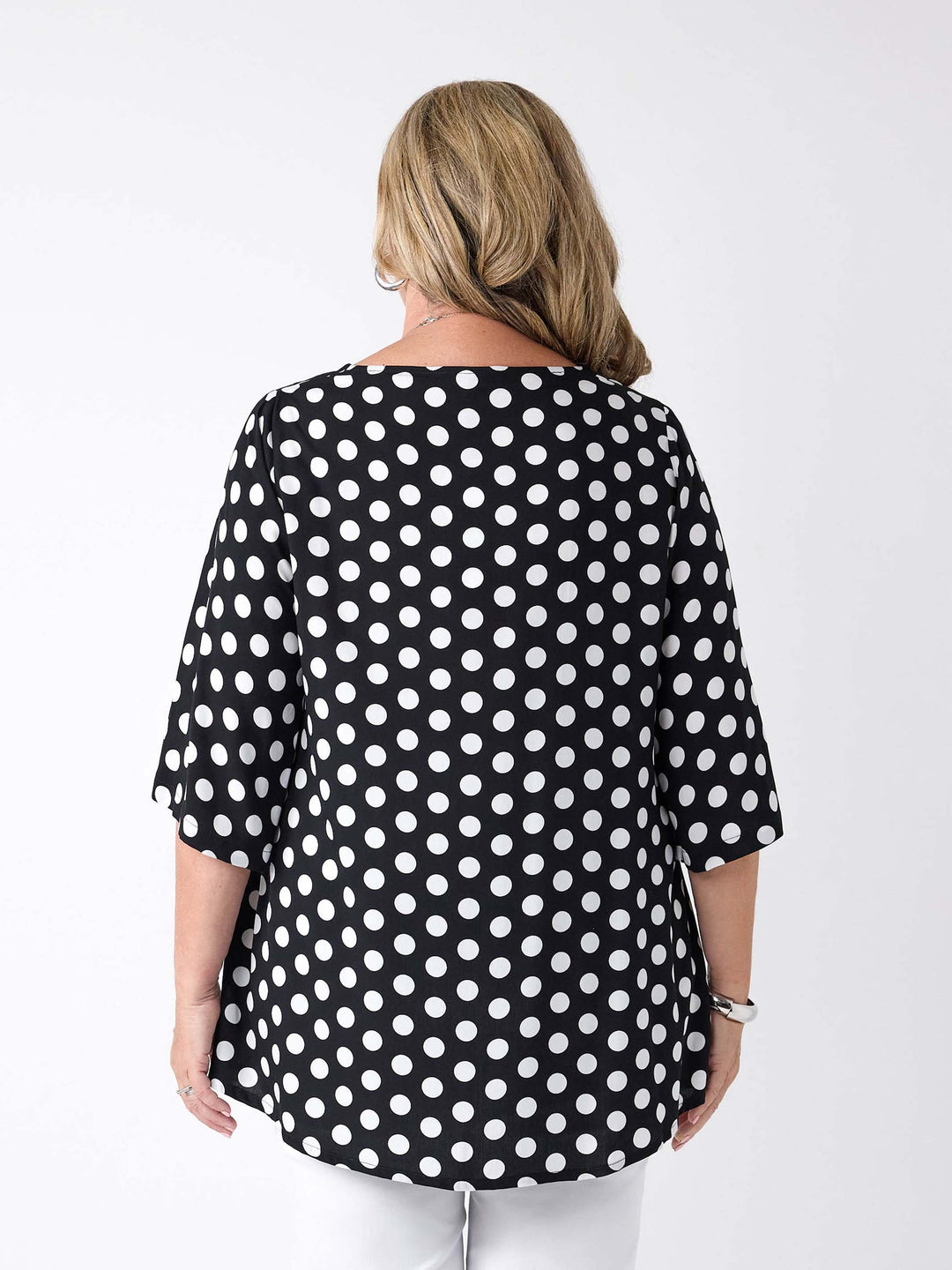 A woman viewed from the back wearing a black V-neck top with white polka dot with three-quarter sleeves, paired with white pants