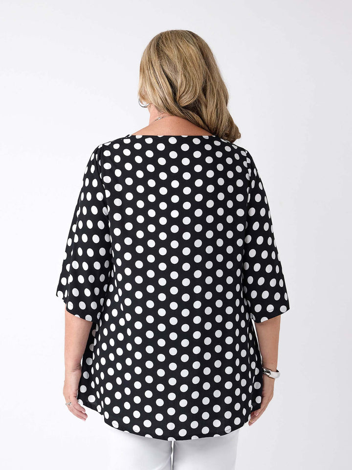 A woman viewed from the back wearing a black V-neck top with white polka dot with three-quarter sleeves, paired with white pants