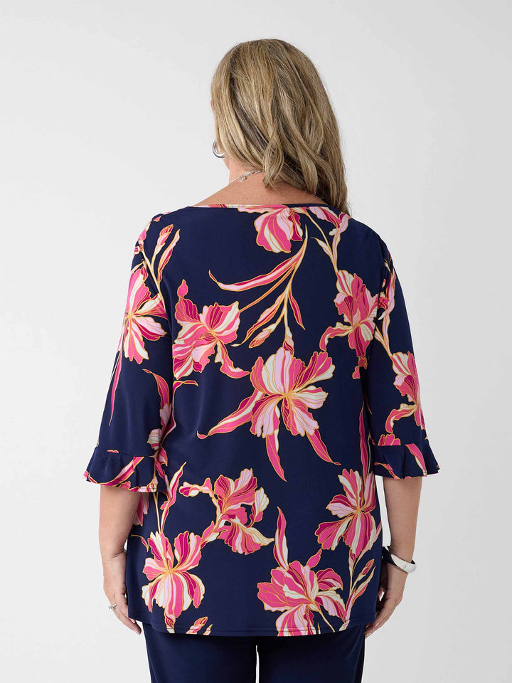 A woman viewed from the back wearing a navy blue top with a bold pink floral print, paired with navy pants
