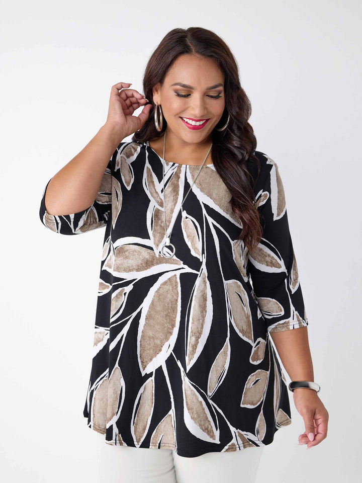 model wearing a three-quarter sleeve tunic top with a beige and white leaf print on black base, paired with white pants