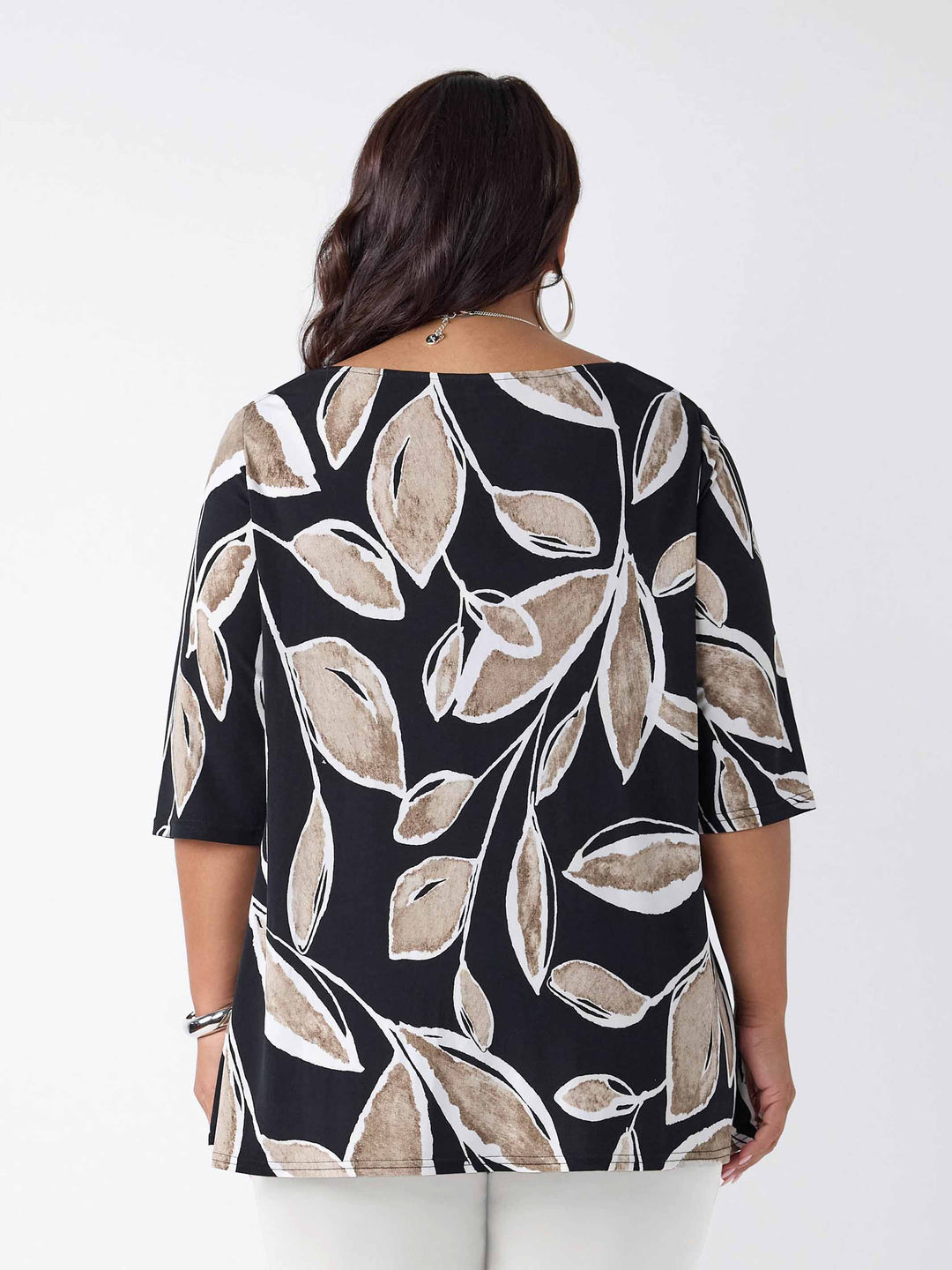 back view of model wearing a three-quarter sleeve tunic top with a beige and white leaf print on black base, paired with white pants