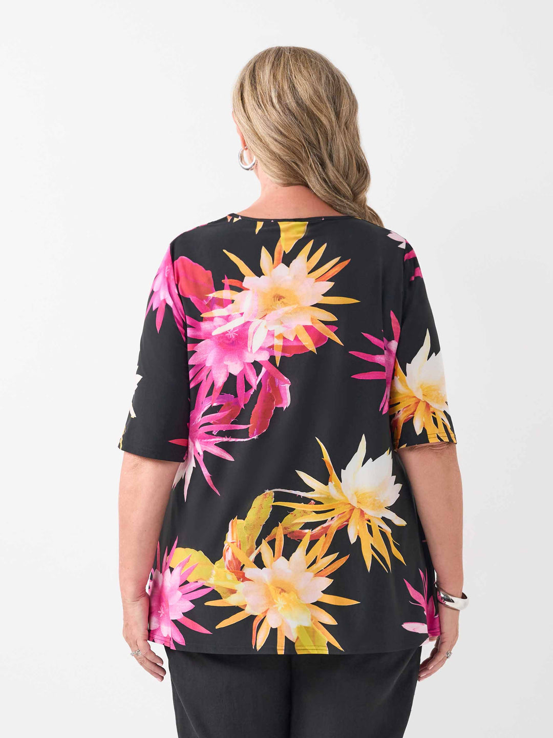 back view of model wearing a black short-sleeve V-neck top with a vibrant tropical floral print in pink and yellow