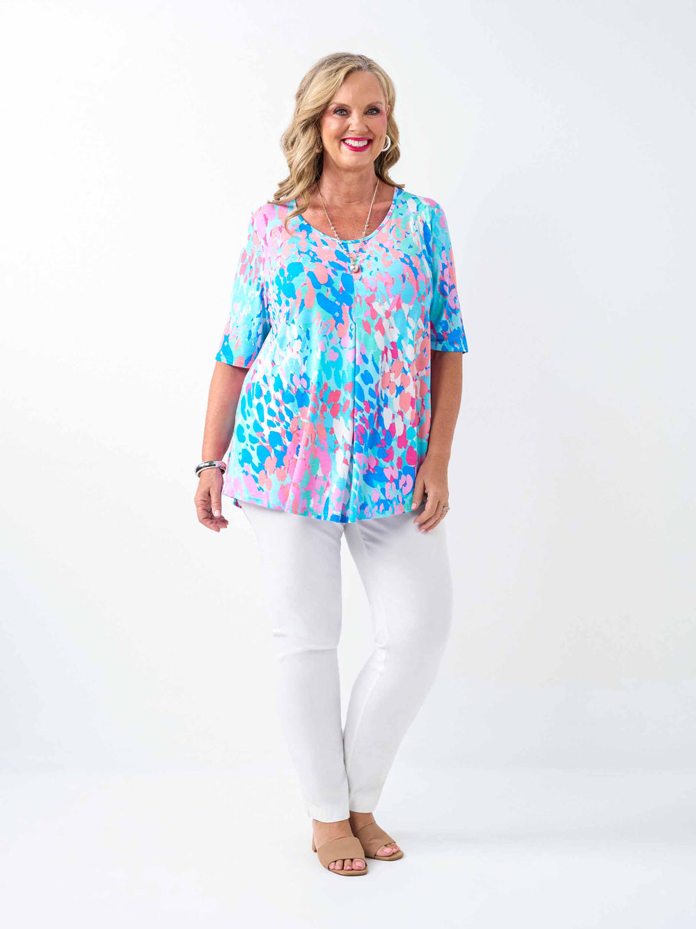 a woman wearing a fresh aqua blue and pink print top with elbow length sleeves and invert pleat, paired with white pant