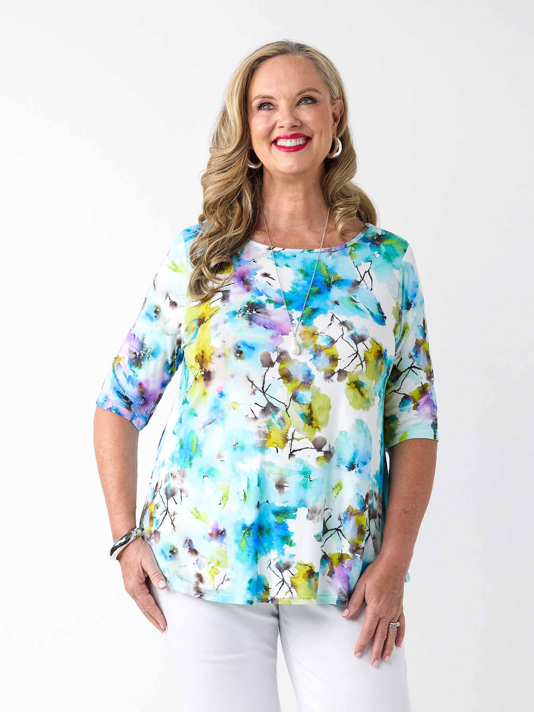A woman wearing a colourful watercolour floral print top in blue with three-quarter sleeves and white pants