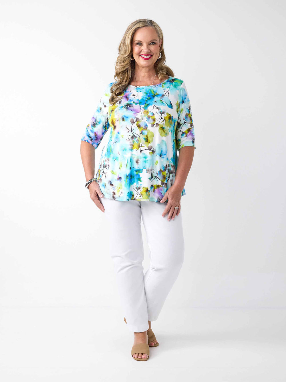 A woman wearing a colourful watercolour floral print top in blue with three-quarter sleeves and white pants