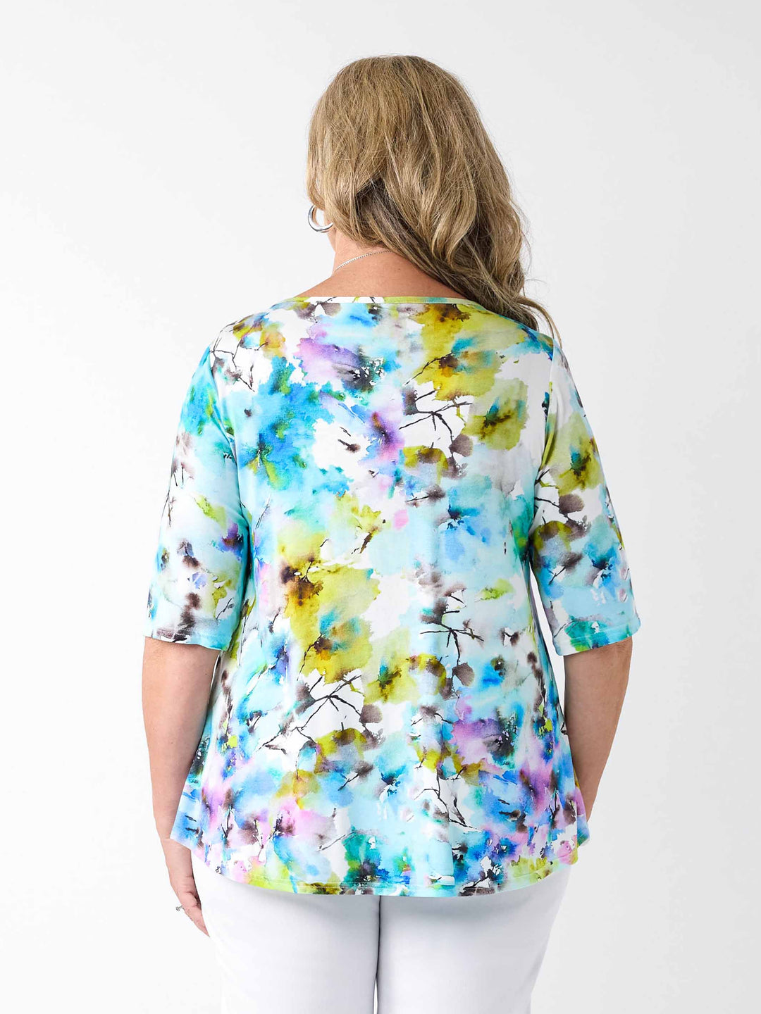 back view of a woman wearing a colourful watercolour floral print top in blue with three-quarter sleeves and white pants