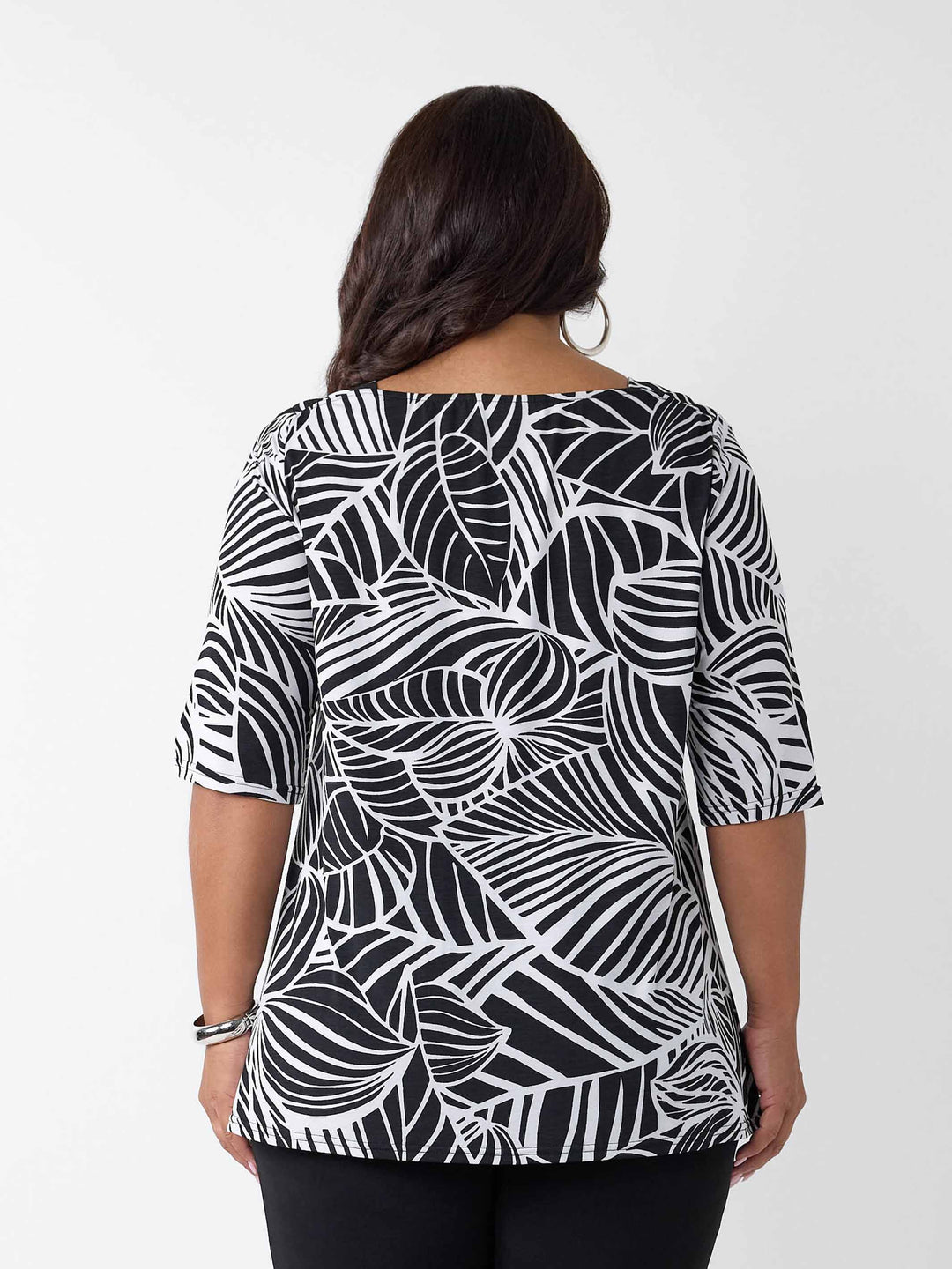 back view of model wearing a black and white tropical leaf print three-quarter length sleeve top paired with black palazzo jersey pant