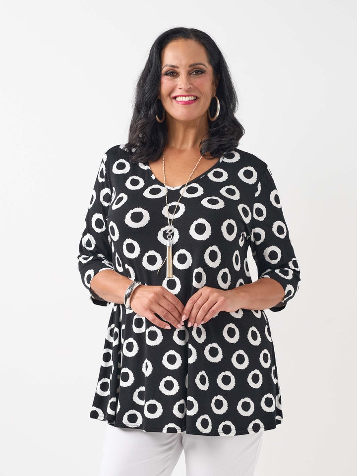 A woman wearing a black three-quarter sleeve top with a white circular dot pattern, paired with white pants