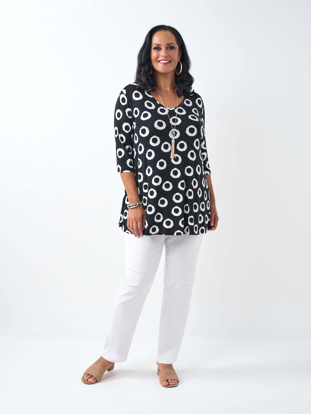 A woman wearing a black three-quarter sleeve top with a white circular dot pattern, paired with white pants