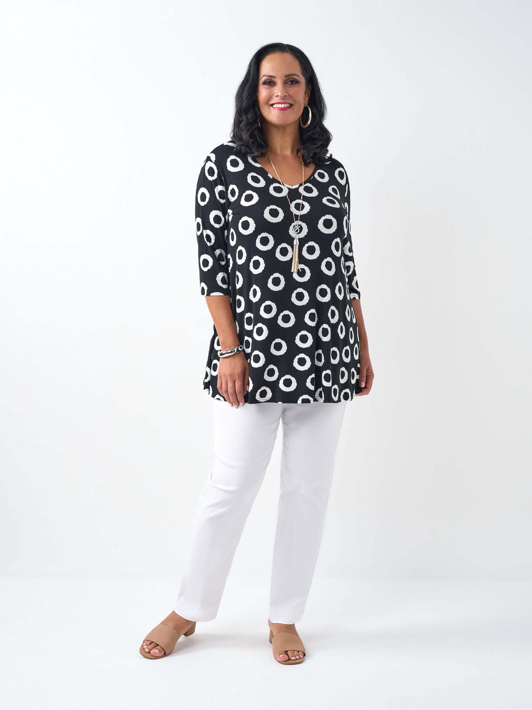 A woman wearing a black three-quarter sleeve top with a white circular dot pattern, paired with white pants